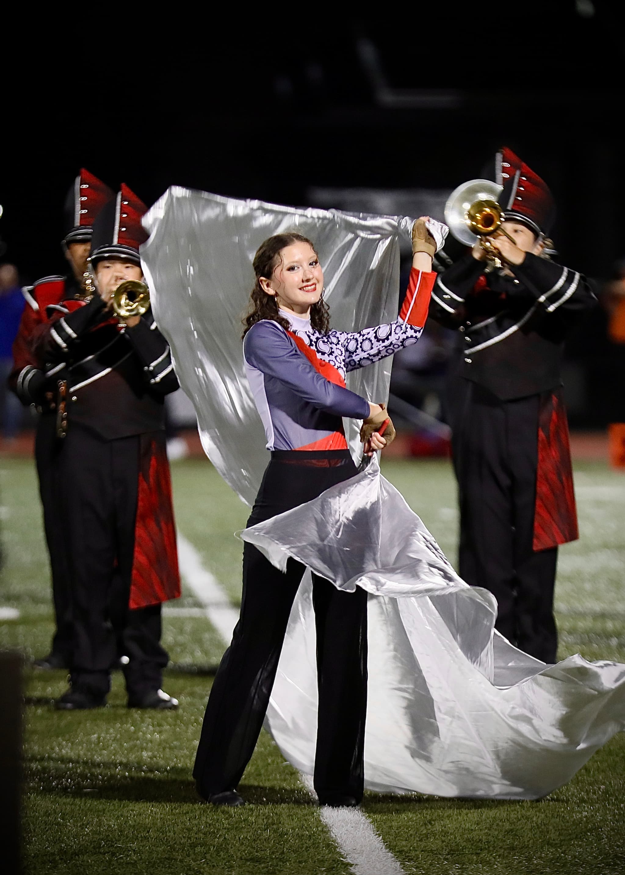 Color guard member spins a silver flag on the football field