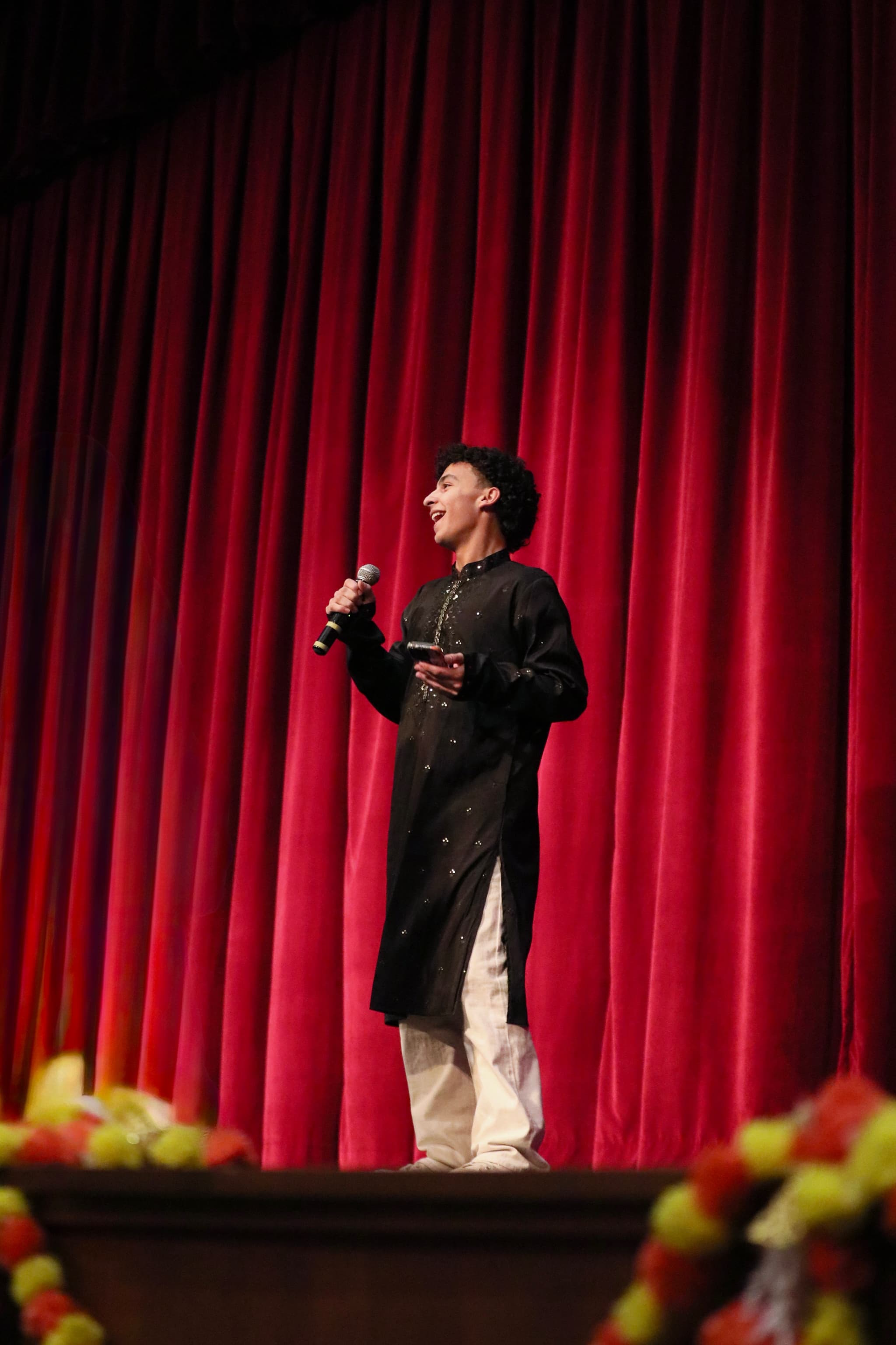 Performer sings on stage before a red curtain
