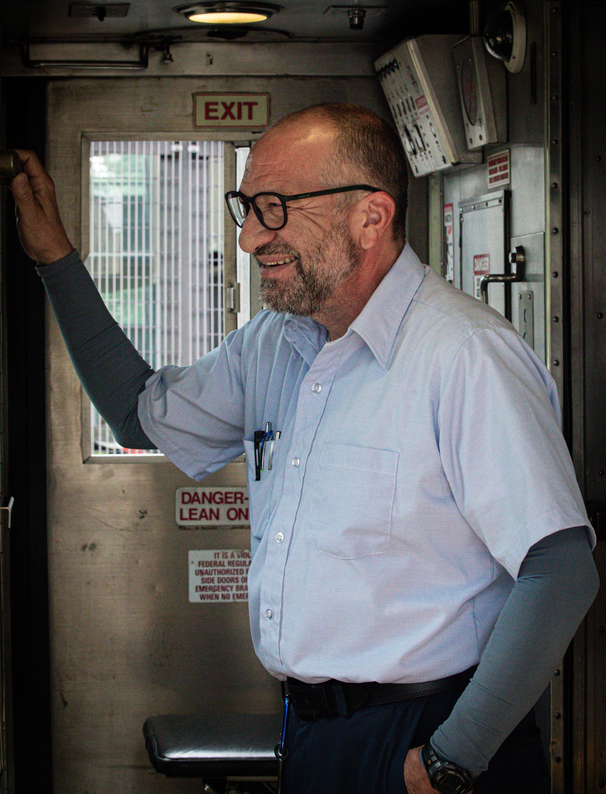 Man in button-down shirt stands in a train car doorway